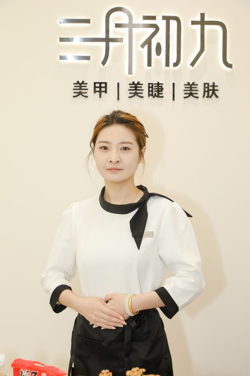 三月初九美甲·新中式精品店的工作人员站在品牌墙前